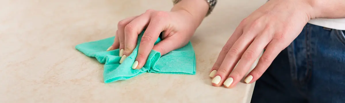 Hand wiping a kitchen countertop with a green microfiber cloth